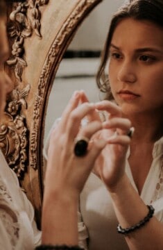 a woman in a white top gazing at herself in the mirror.