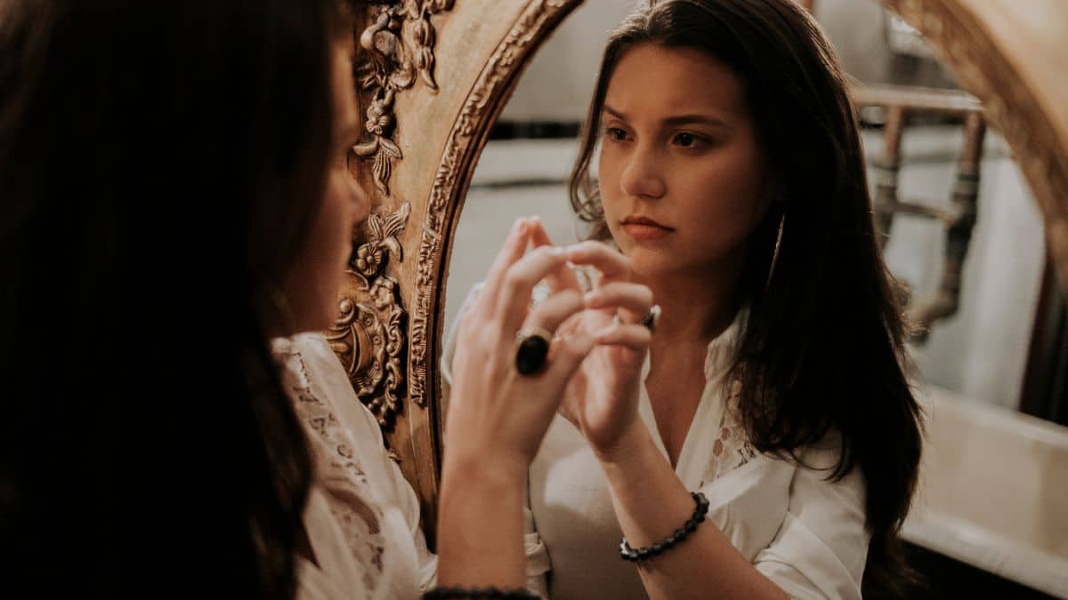 a woman in a white top gazing at herself in the mirror.