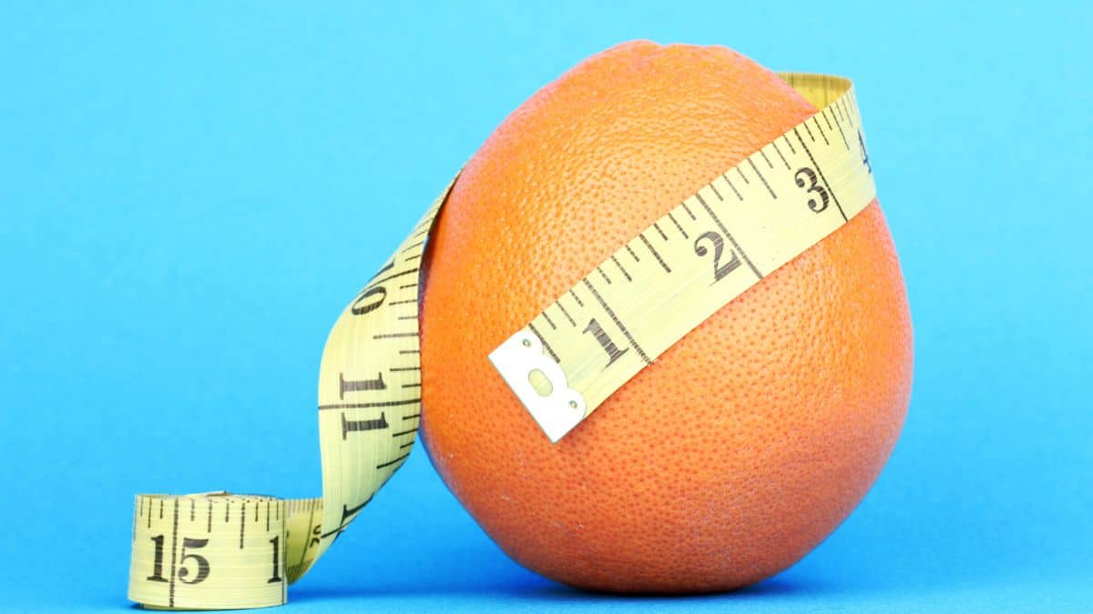 an orange with a tape measure wrapped around it as though it's measuring it's waist.