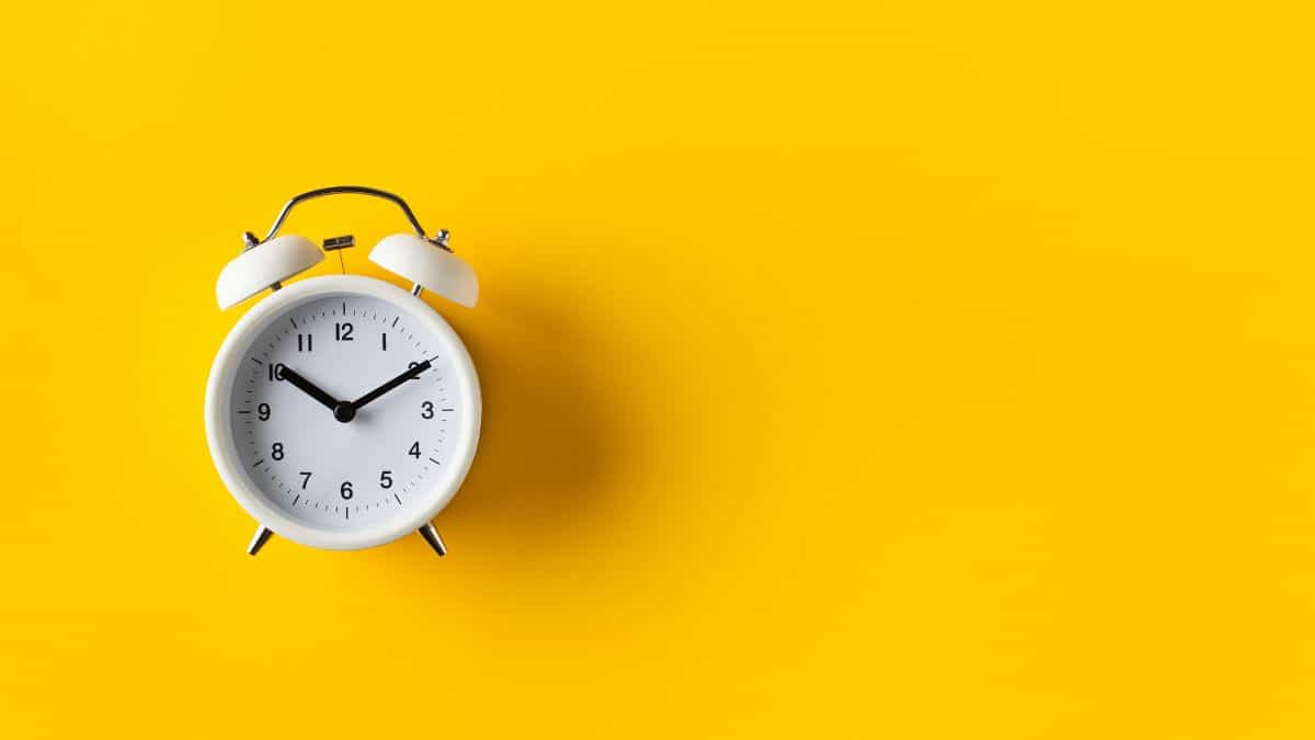 a white old fashioned clock against a yellow background.