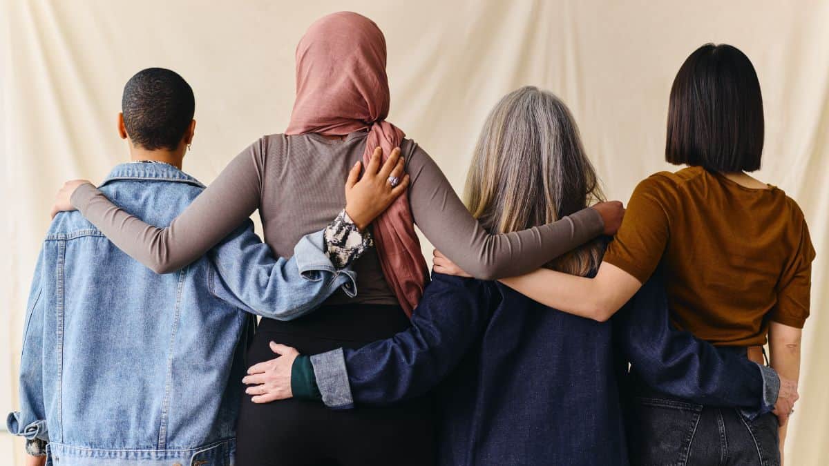 four women back facing embracing one another.