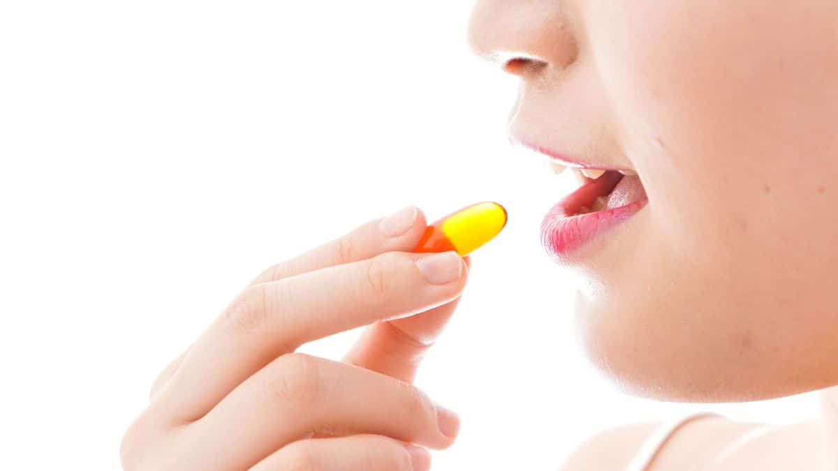 A close view of a woman putting an oval pill in her mouth, similar to plexus.
