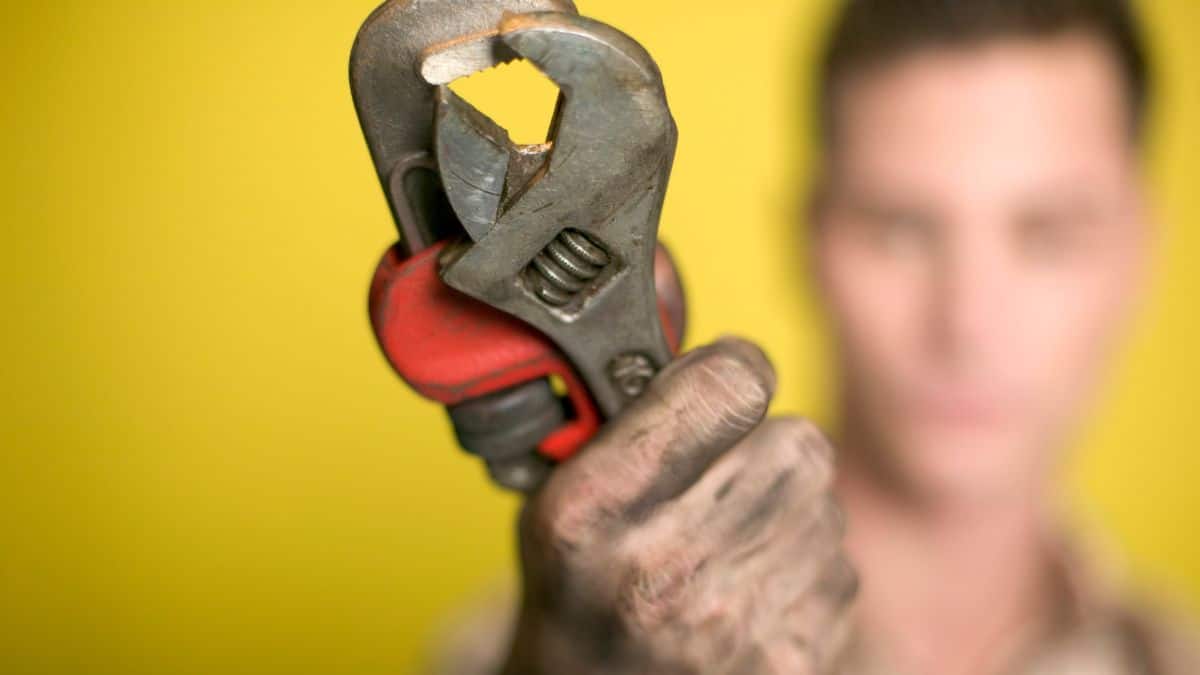 A man holding a wrench in front of a yellow background.
