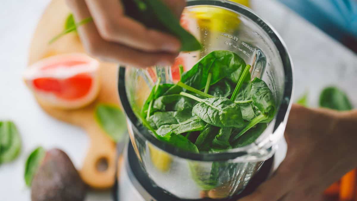 close up of blender with green smoothie ingredients.