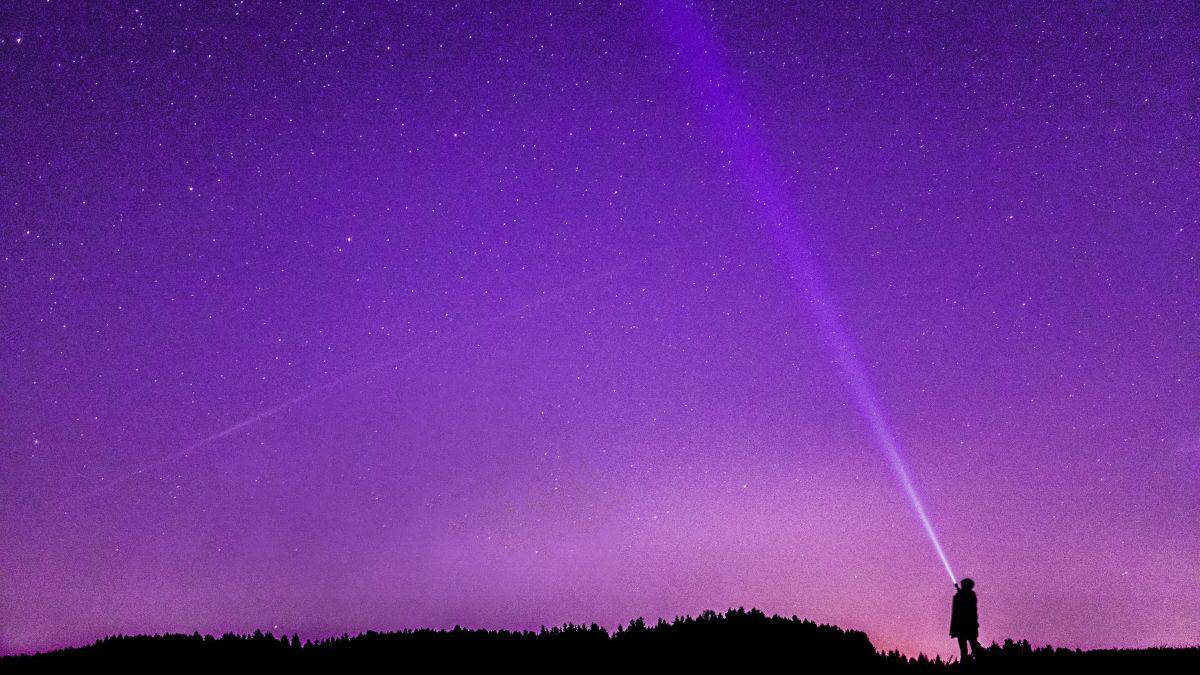 Silhouette of a person shining a flashlight into a starry sky.