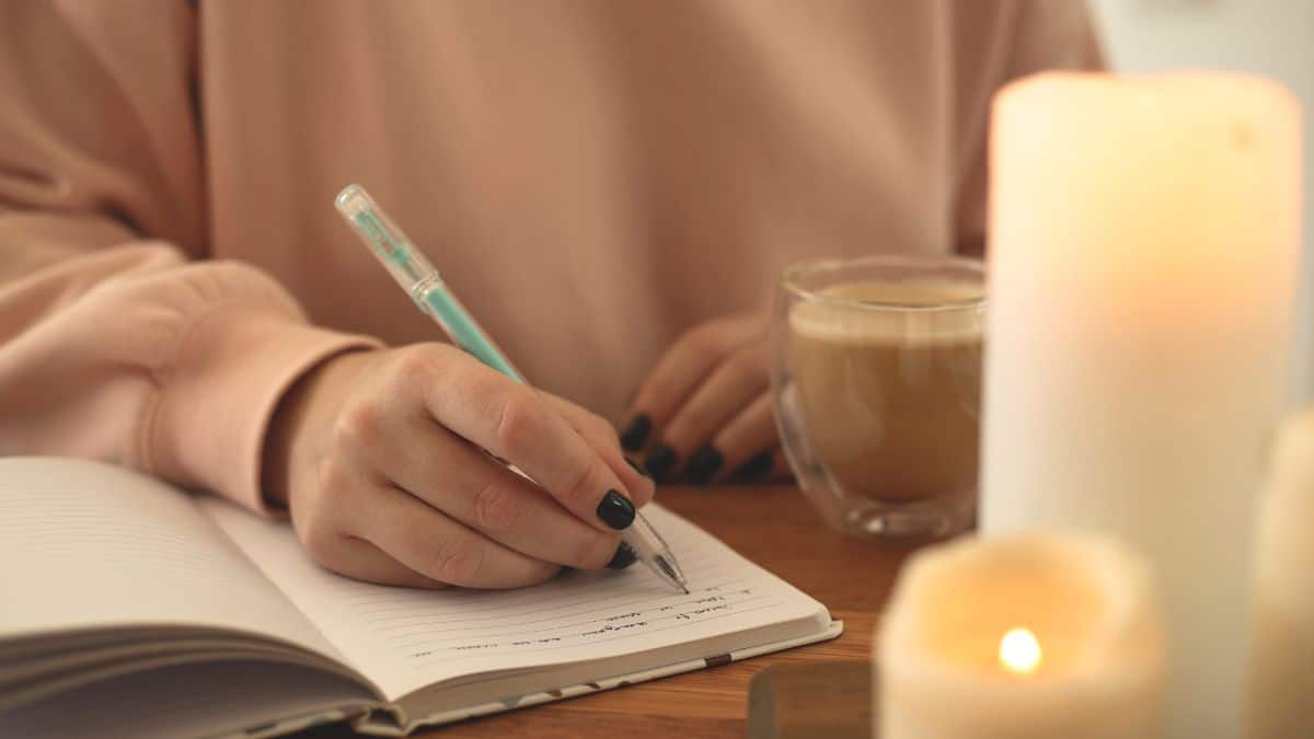 A woman getting ready to write in her journal; a cup of coffee and candles are nearby.