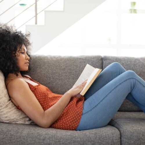 a woman reading an intuitive eating book on a gray couch.