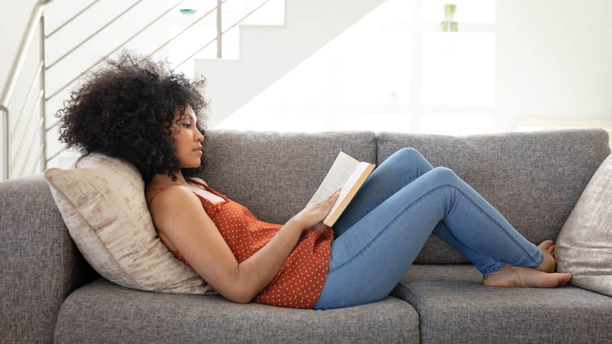 a woman reading an intuitive eating book on a gray couch.