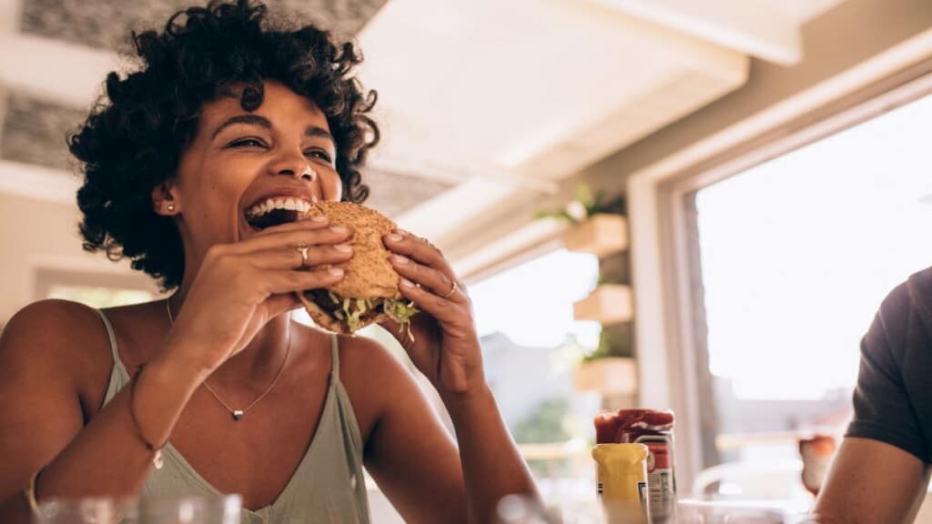 a woman mindfully eating a sandwich with a smile on her face.