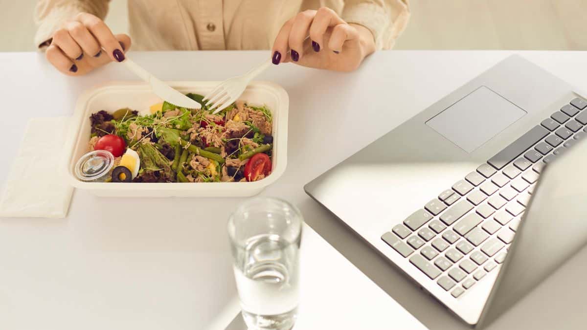 a working lunch with a takeout container, glass of water, and laptop.