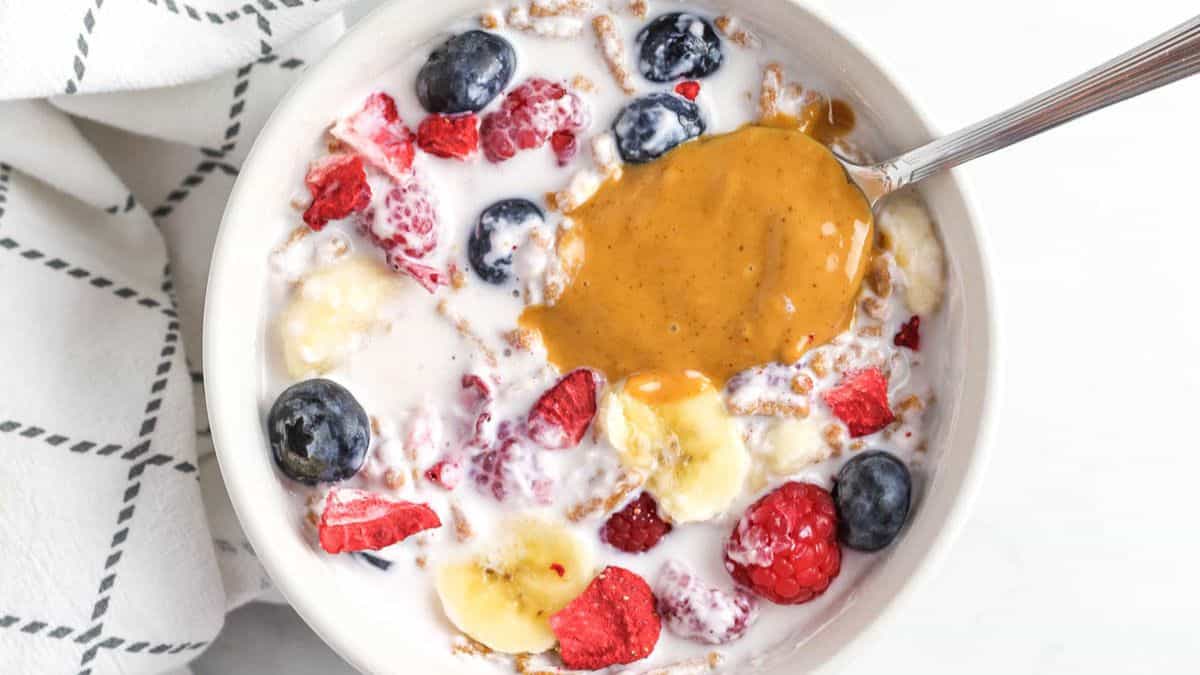 a bowl of smoothie cereal with berries, yogurt, and peanut butter on a spoon.