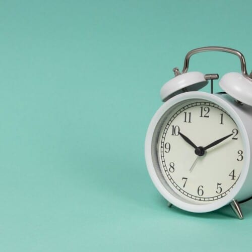 a white old fashioned alarm clock with blue background.
