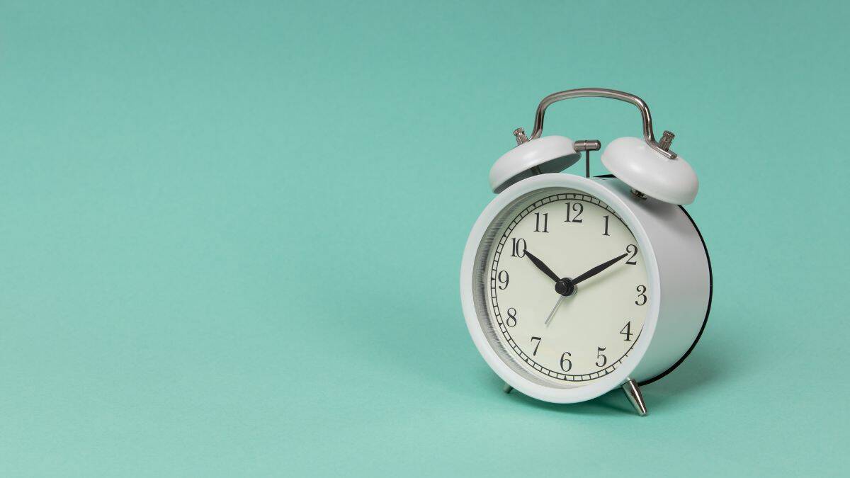 a white old fashioned alarm clock with blue background.