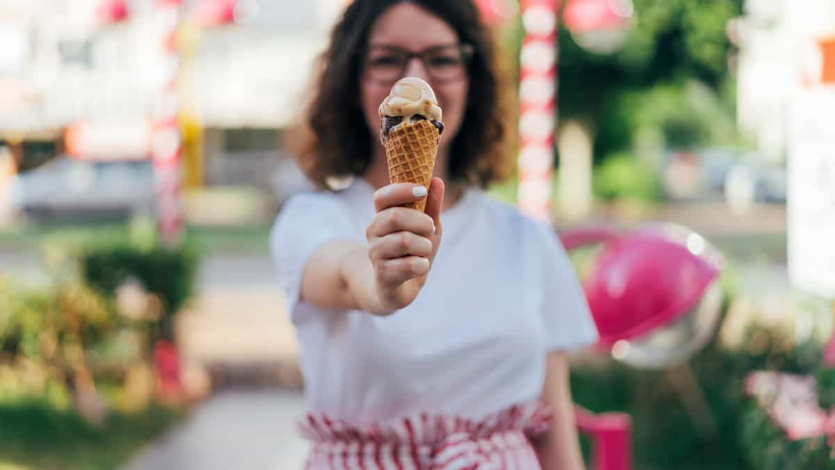 happy woman holding ice cream cone in front of her on a summer day.