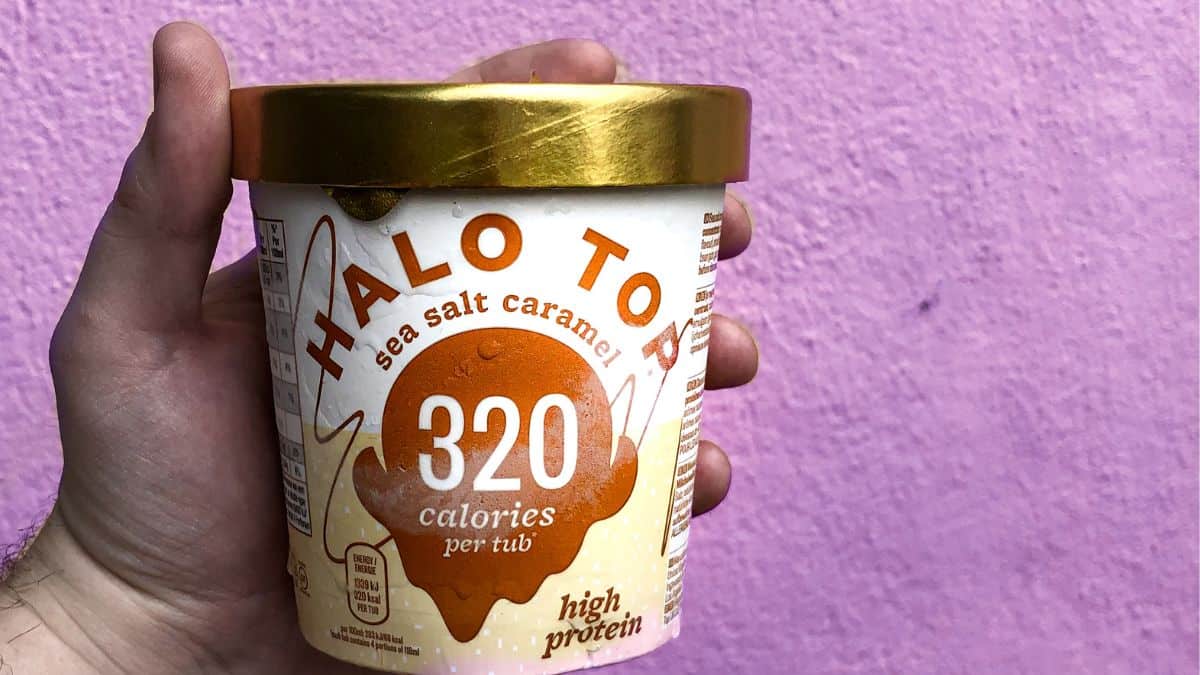 man holding low calorie pint of ice cream against purple wall.