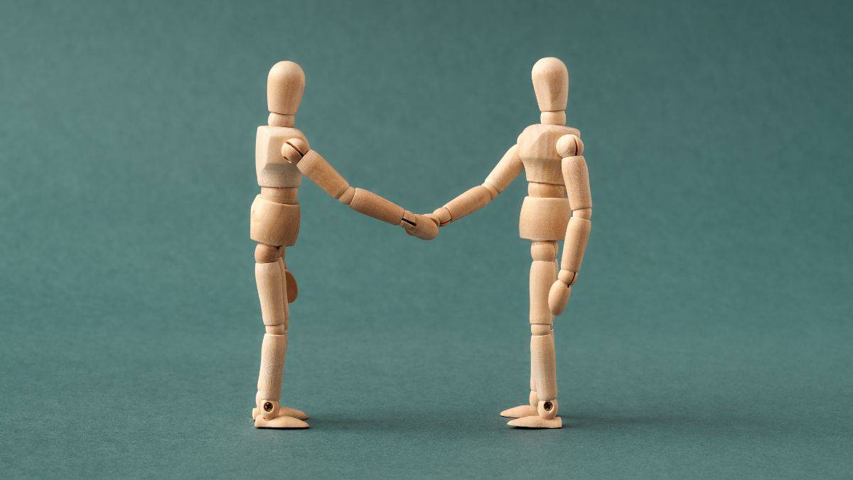 two wood sculpting figures shaking hands.