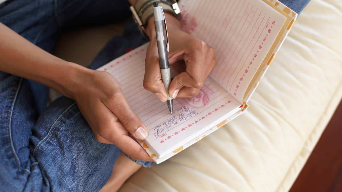 woman wearing jeans writing in journal in her lap.
