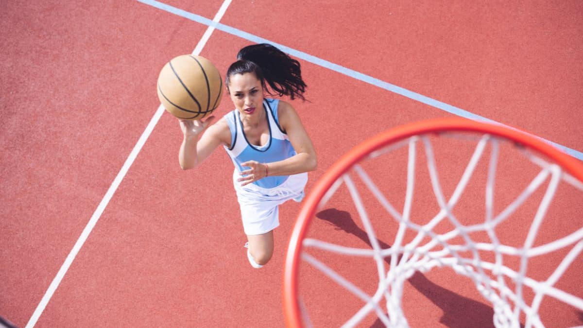 woman shooting a basketball in a hoop on basketball court.